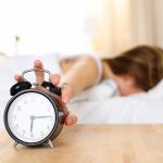 A woman laying in bed with an alarm clock.